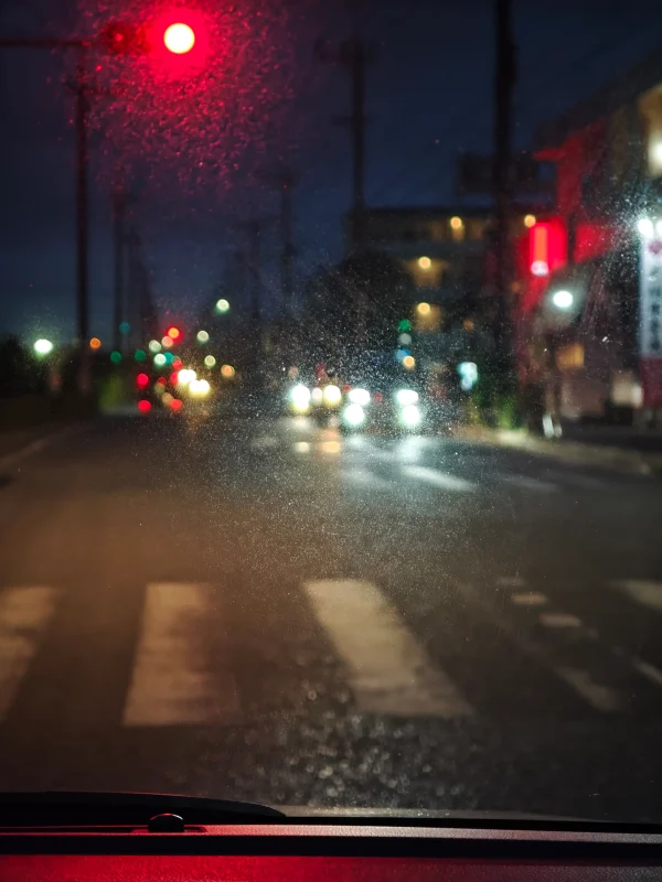 Oil film on a car windshield causing blurry night driving visibility in rain